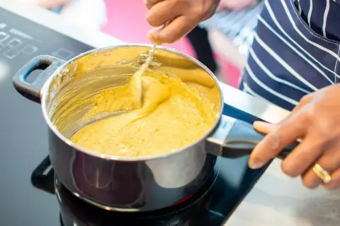 Ręce mieszają gęsty, żółty sos w garnku na płycie indukcyjnej. To idealny moment, by dowiedzieć się, jak zagęścić sos śmietaną i mąką.