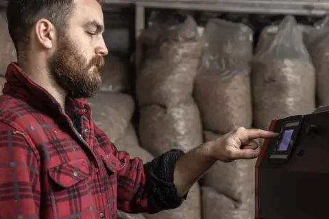 Mężczyzna w kratę reguluje panel sterowania kotła na pellet. To przykład modulacji kotła, czyli dostosowania jego pracy do potrzeb.