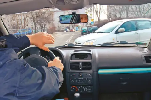 Widok z wnętrza samochodu na kierowcę trzymającego kierownicę i drogę z innymi autami.