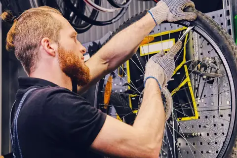 Mechanik w rękawiczkach naprawia **detkę** w rowerze, używając łyżki do opon.