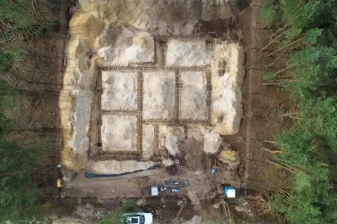 Budowa fundamentów domu w lesie. Widać zbrojenie i szalunki. W tle drzewa. To etap prac poprzedzający badania geotechniczne gruntu.