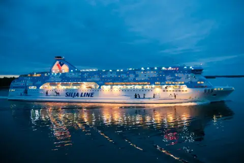 Prom Silja Line Galaxy płynie po wodzie o zmierzchu, odbijając światła w mroku. Podróż z Rygi do Helsinek zaczyna się!