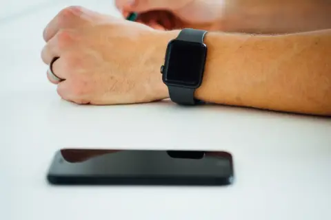 Czarny smartwatch na nadgarstku i leżący obok smartfon. Dowiedz się, jak włączyć bluetooth w zegarku, by połączyć go z telefonem.