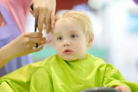Mały chłopiec z blond włosami otrzymuje swoją pierwszą fryzurę. Włosy są delikatnie cięte, tworząc urocze fryzury dla rocznego chłopca.