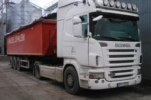 Biała Scania R420 z naczepą "Handel Opałem" stoi przy silosach. Zastanawiasz się, ile kosztuje nowa Scania?