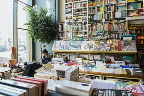 Nadprodukcja książek sprawia, że bestsellery żyją krócej. W księgarni pełnej tytułów, młoda kobieta przegląda telefon.