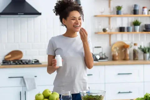 Mujer sonriente en cocina, tomando suplemento. El zinc para que sirve en la mujer es clave para su bienestar general y salud.