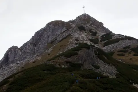Grupa turystów wspina się po skalistym zboczu. Czy Giewont jest trudny? Trasa wydaje się wymagająca, ale widok na szczyt z krzyżem zachęca do dalszej wędrówki.