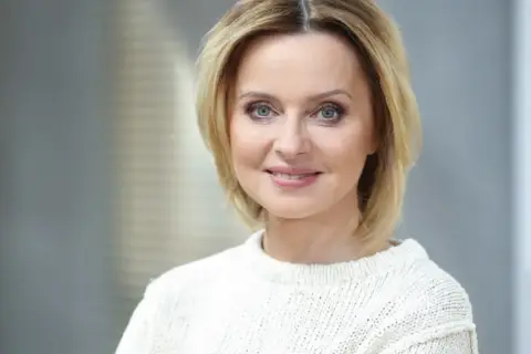 Jolanta Pieńkowska w białym swetrze, z uśmiechem na twarzy. Spekulacje o jej operacje plastyczne krążą od lat.