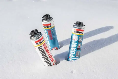 Trzy puszki pianki montażowej zimowej Soudal w śniegu. Pianka "Maxi Express" i "Classic" obok siebie, a dalej "Foam".