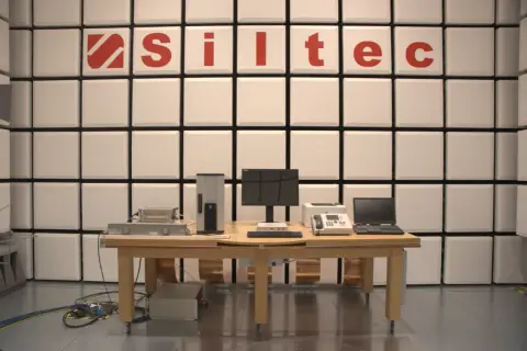 Laboratorium testowe z urządzeniami elektronicznymi i logo "Siltec". W tle ściana z paneli akustycznych, chroniąca przed zakłóceniami, jak podczas burzy (tempest).