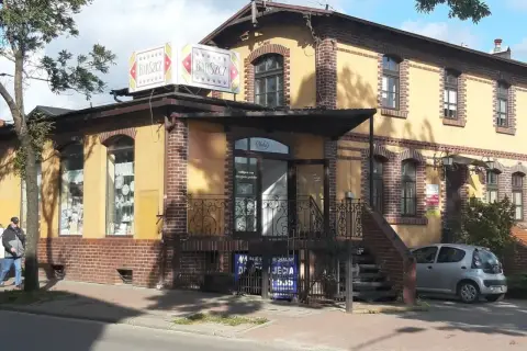 Bar "Barszcz" w Wejherowie. Żółty budynek z ceglanymi zdobieniami, szyldem "Barszcz" i małym srebrnym samochodem.