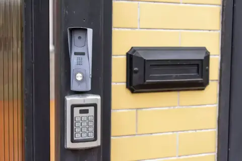 Nowy domofon z klawiaturą kodową i skrzynką na listy na żółtej ścianie bloku.