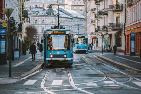 Niebieskie tramwaje na ulicy w Oslo, z budynkami po bokach.