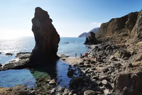 Gente disfrutando de la **playa del Sombrerico**, con sus rocas y aguas cristalinas. ¡Un lugar para guardar en la memoria!