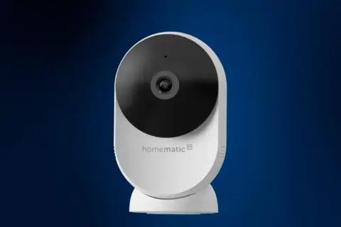 Weiße Homematic IP Überwachungskamera mit schwarzem Objektiv vor blauem Hintergrund.