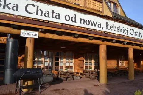 Drewniana, łebska chata z banerem "od nowa, Łebskiej Chaty". Przed wejściem grill i stoliki.