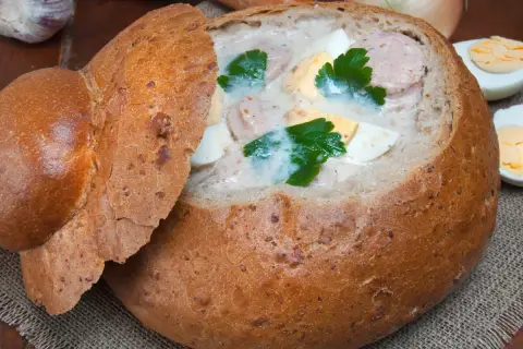 Pyszny żurek w chlebie, z kiełbasą i jajkiem, ozdobiony natką pietruszki. Idealny na polski obiad.