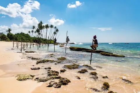 Rybołówka na palach w Mirissa, Sri Lanka. Trzech rybaków łowi ryby siedząc na drewnianych słupach w płytkiej wodzie.