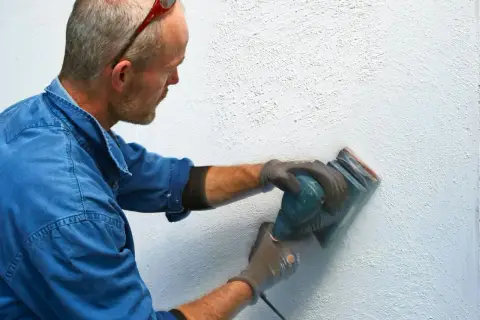 Man slipar en vägg med en excenterslip för att få bort slipdamm innan målning.