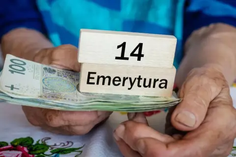 Dłonie trzymają stos banknotów i drewniane klocki z napisem "14 Emerytura".