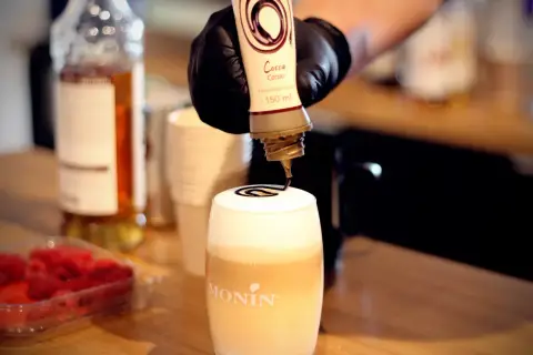 Barista ozdabia gorącą czekoladę do picia syropem kakaowym.