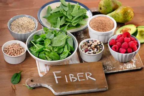 En skärbräda med texten "FIBER" omgiven av skålar med bönor, linser, spenat, hallon, päron, avokado och korn.