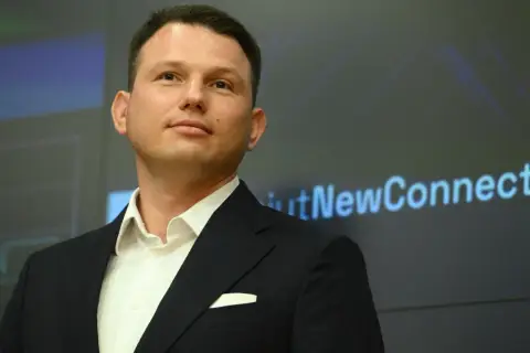 Kto finansuje luksusowe spotkania wyborcze Mentzena w największych miastach Polski? Mężczyzna w garniturze na tle ekranu z napisem "NewConnect".