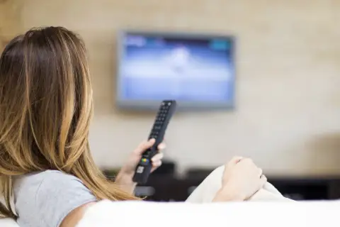 Kobieta z pilotem w ręku ogląda telewizję, ciesząc się swoim abonamentem radiowo-telewizyjnym.