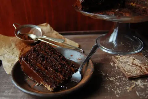 Wilgotny tort czekoladowy z kremem nutella, posypany kakao, czeka na widelca. Obok kawałek czekolady.