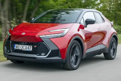 Czerwona Toyota C-HR 2020 z czarnym dachem pędzi po drodze, otoczona zielenią drzew.