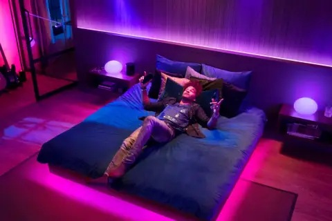 Mann liegt im Bett, umgeben von Philips Hue Lichtern, die sich im Takt von Spotify-Musik synchronisieren.