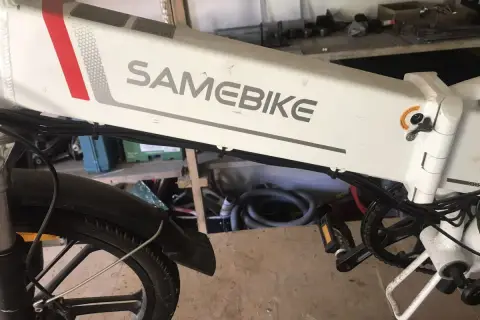 Biały rower elektryczny SAMEBIKE, z czerwonym i szarym paskiem, stoi w warsztacie. Wspomaganie nie działa, co jest frustrujące.