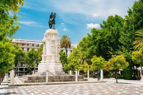 Majestuoso monumento ecuestre, una de las **estatuas en Sevilla**, rodeado de árboles frondosos y un cielo azul vibrante.