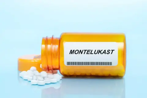 Pomarańczowa butelka z tabletkami montelukast, kilka białych tabletek rozsypanych obok.
