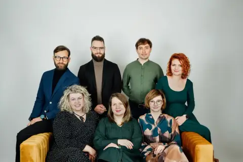 Grupa siedmiu psychoterapeutów, cztery kobiety i trzech mężczyzn, pozuje do zdjęcia na kanapie.