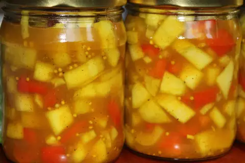 Dwa słoiki z marynowaną cukinią w zalewie curry z kawałkami papryki i gorczycą.