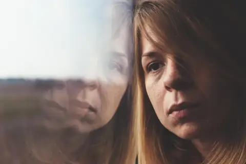 Portret kobiety z widocznym odbiciem w szybie, sugerującym refleksję lub rozdwojenie.