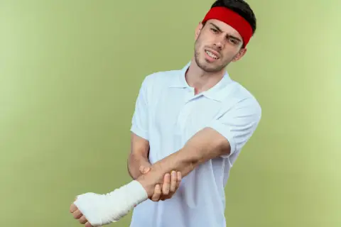 Mężczyzna w czerwonej opasce na głowie i białej koszulce z bólem trzyma rękę w bandażu, jakby po odwróconym teście Cozena.