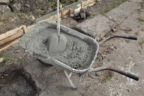 Taczka z betonem i łopatą, gotowa do wylania ławy fundamentowej. Wymiary ławy fundamentowej są kluczowe dla stabilności konstrukcji.