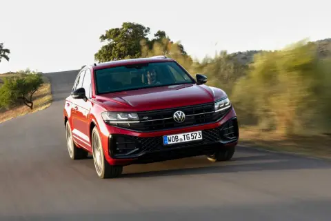Czerwony Volkswagen Touareg 2024 pędzi po krętej drodze wśród wzgórz.