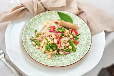 Ein bunter Thunfisch-Bohnen-Salat, italienisch inspiriert, mit grünen Bohnen, roten Zwiebeln und Tomaten auf einem Teller mit grünem Muster.
