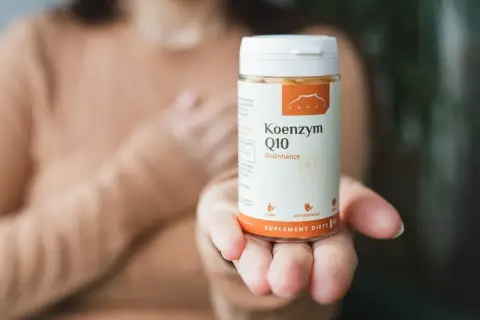 Dłoń trzyma buteleczkę suplementu diety z koenzymem Q10.
