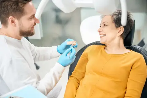 Dentista mostra un modello di denti a una paziente sorridente, discutendo di impianti dentali per un sorriso perfetto.