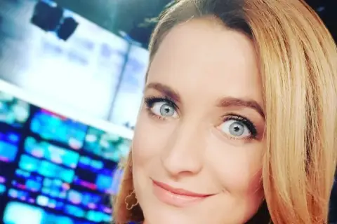 Dagmara Kaczmarek Szalkow z TVN Fakty z błękitnymi oczami i blond włosami, w tle ekrany.