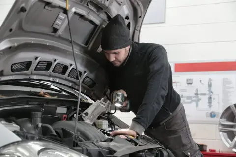 Mechanik samochodowy z latarką bada silnik. Zastanawiasz się, ile zarabia elektronik samochodowy?