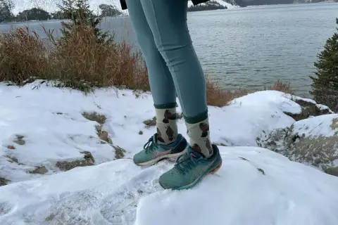Wygodne leginsy w góry i buty do biegania na śniegu. W tle jezioro i ośnieżone szczyty.