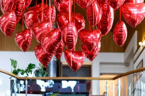 Mnóstwo błyszczących, czerwonych balonów w kształcie serc i owali, tworzących romantyczne ozdoby walentynkowe diy.