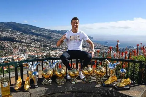 Cristiano Ronaldo z pięcioma złotymi piłkami, symbolizującymi jego sukcesy.