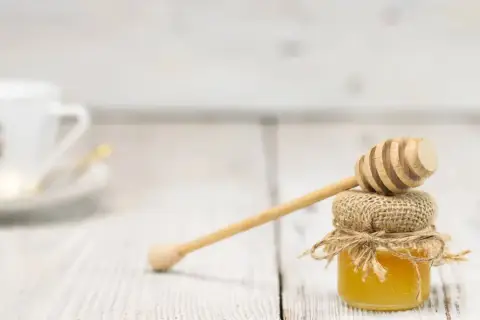 Mały słoiczek miodu, naturalnego źródła węglowodanów, z drewnianą chochlą. W tle biała filiżanka.